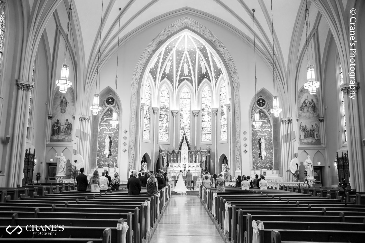 Black and white photo showing the interior of St. Peter and Paul Church in Naperville with the bride and groom kneeling at the altar