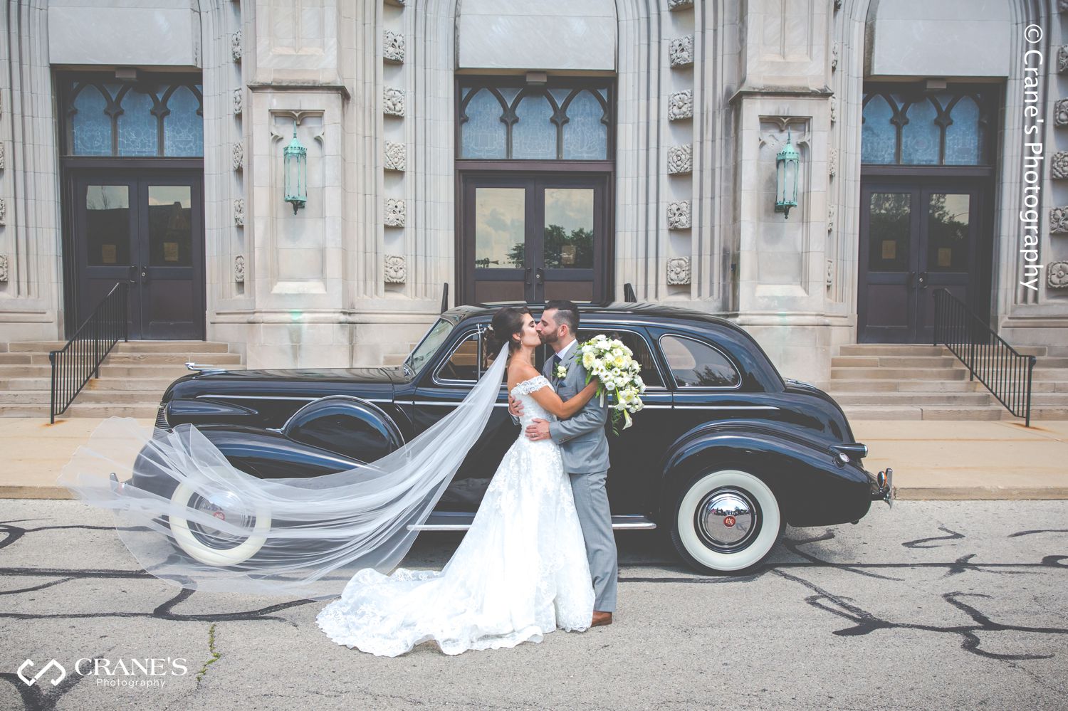 Bride and groom kiss in front of their vintage car in front of St. Peter and Paul Church in Naperville.