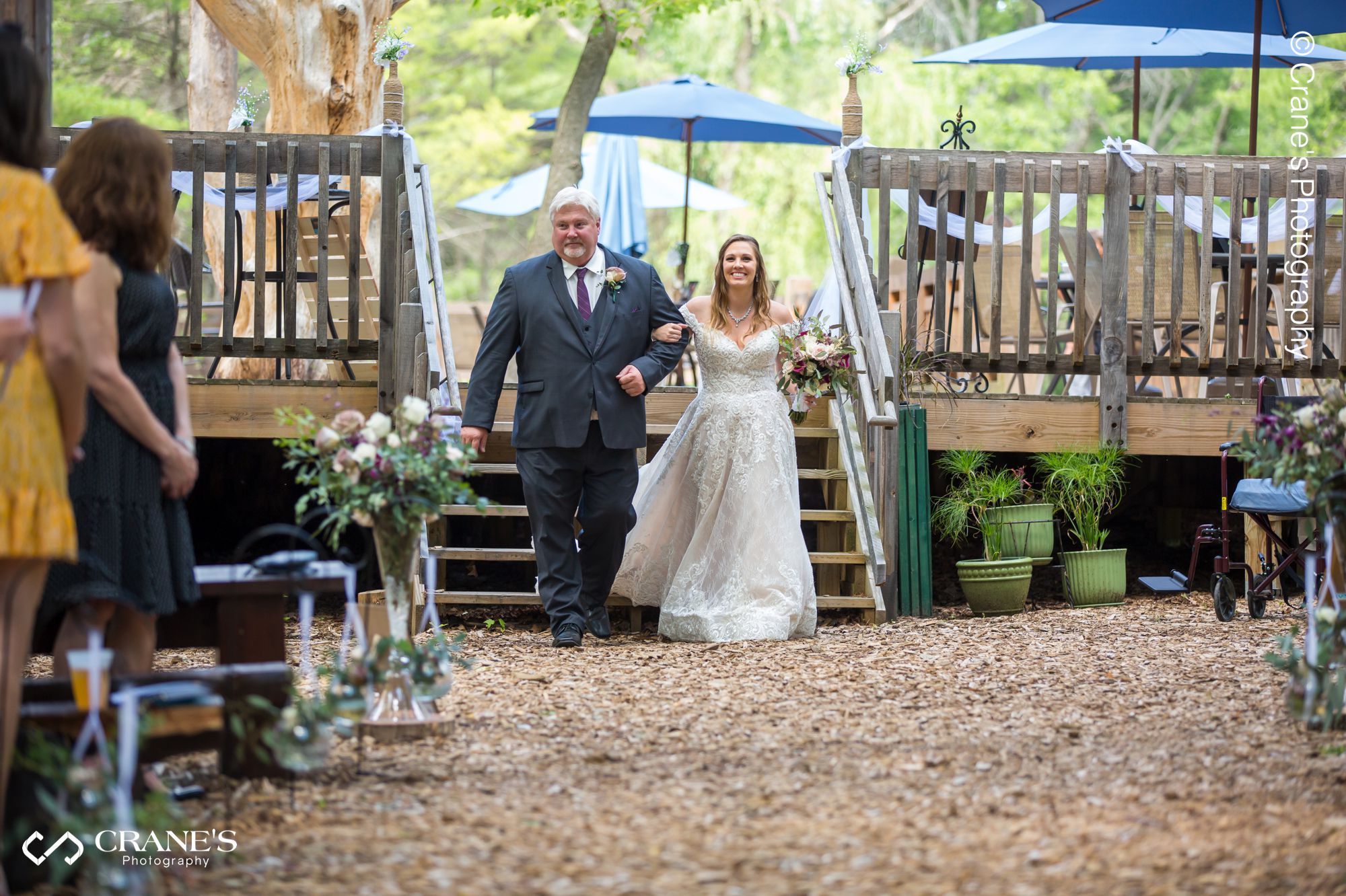 A bride walks down the aisle with her dad during an outdoor wedding ceremony at The Swan Barn Door