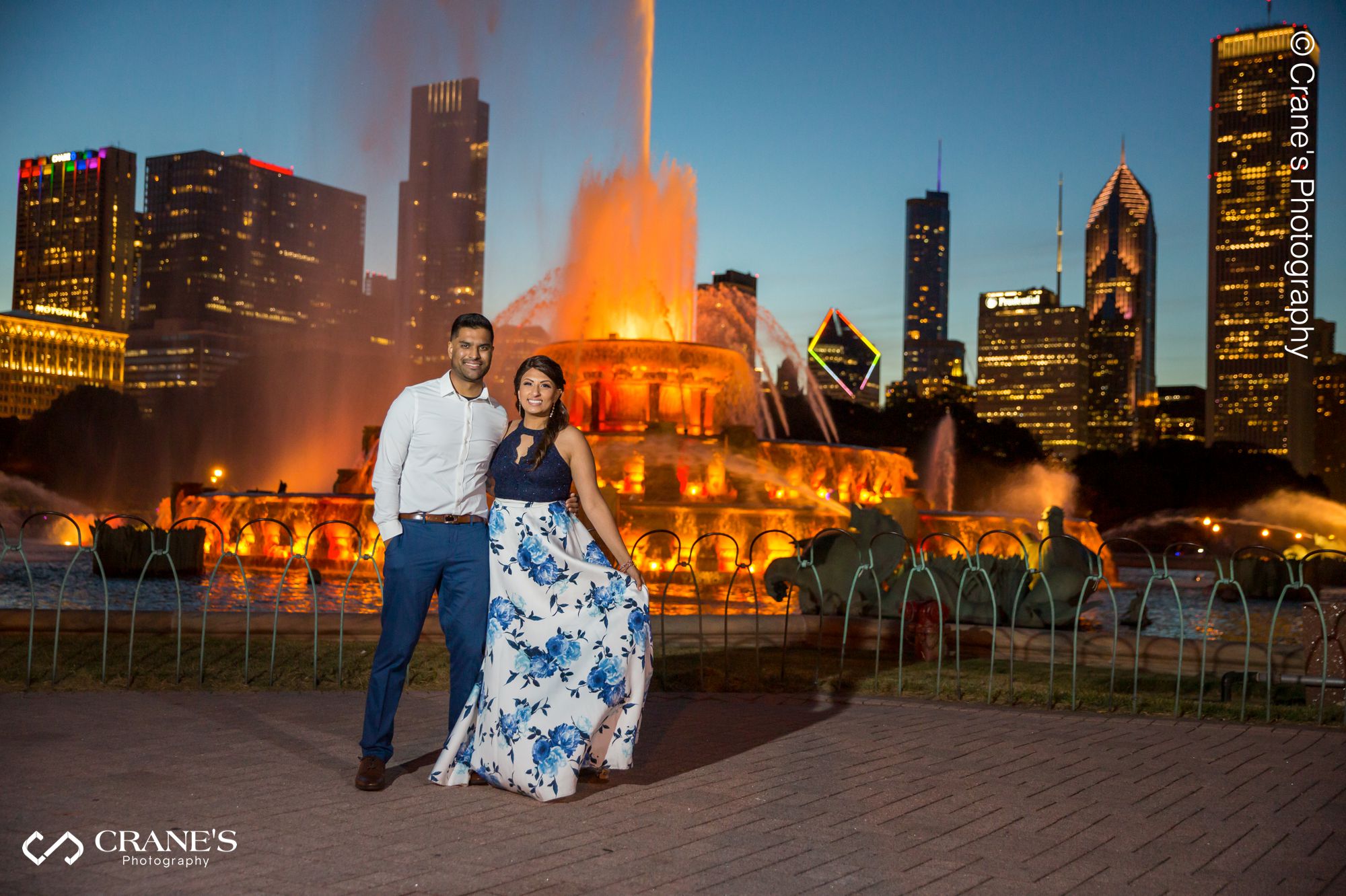 An Indian couple wearing blue outfits taking an engagement photos at the Buckingham Fountain at night