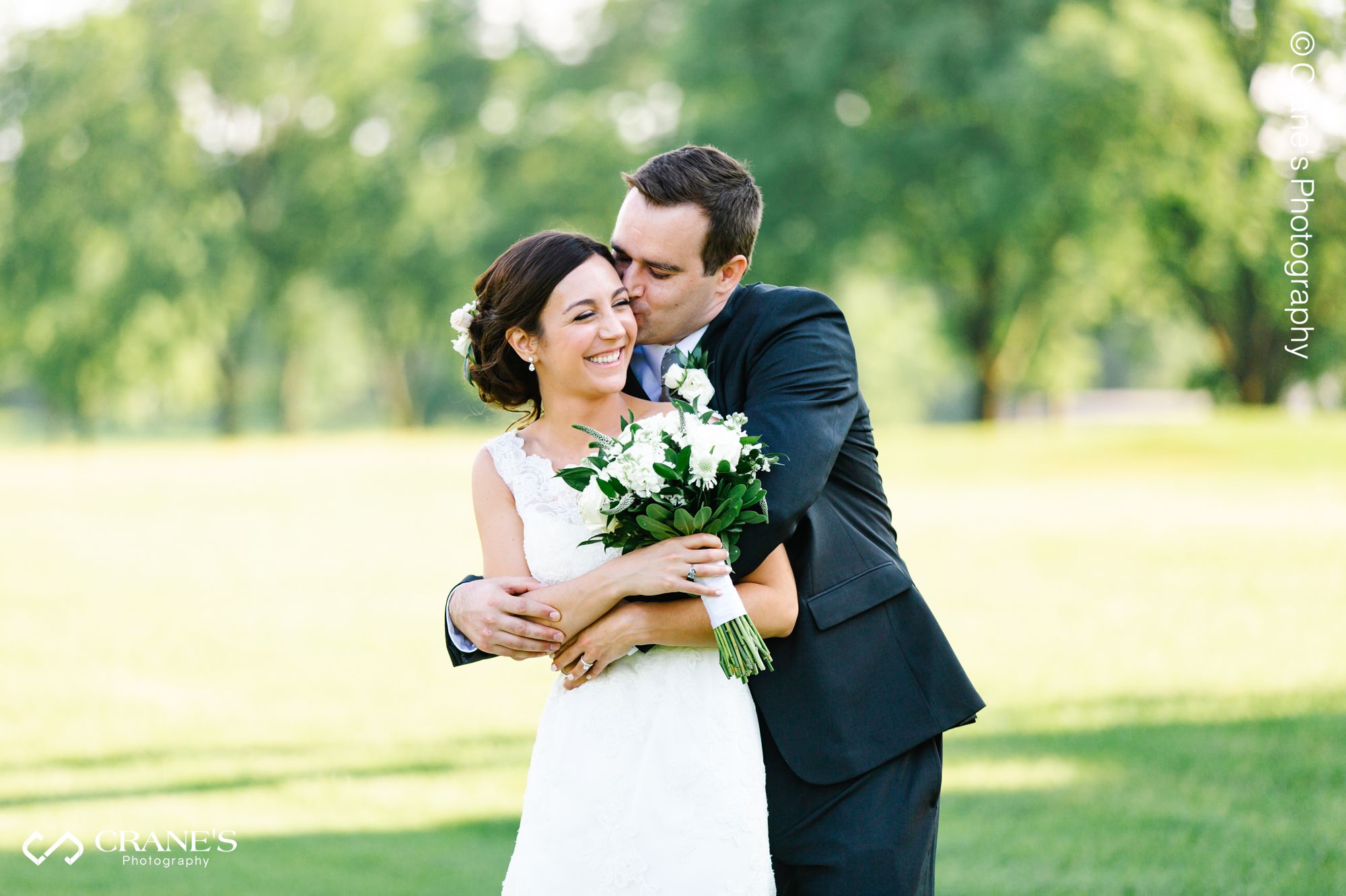 Groom kissing her bride on the cheek while she is laughing at La Grange Country Club