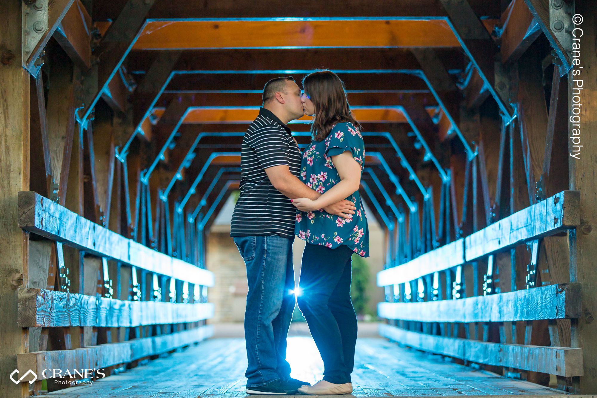 Creative lighting of an engaged couple kissing at the bridge at the Naperville Riverwalk