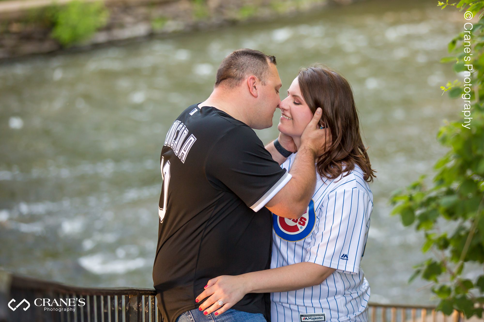 A couple wearing baseball jerseys kissing with a river in the background
