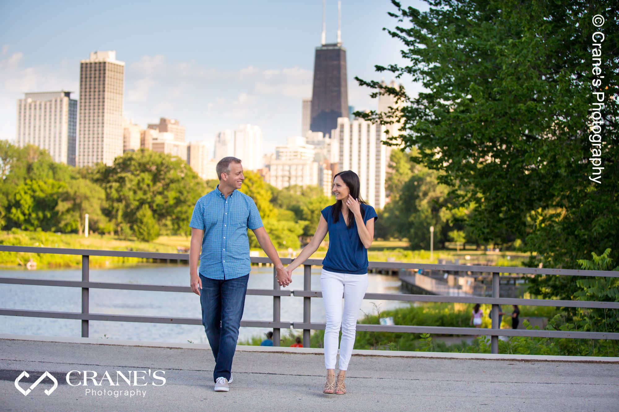 An engagement session photo of couple walking hand in hand with the city of Chicago in the background