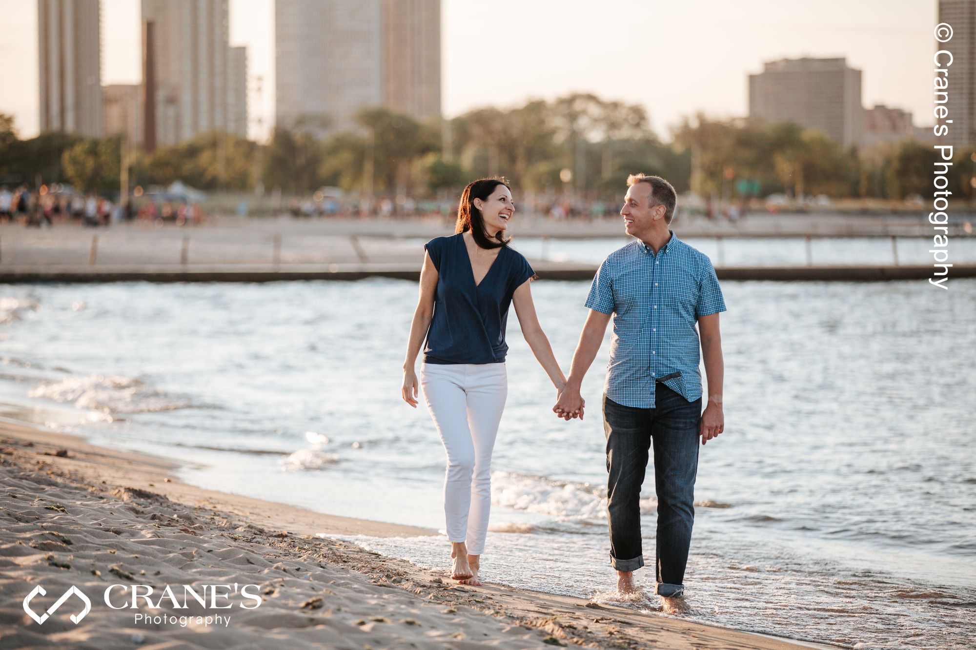 An engaged couple walk hand in hand on a beach near Chicago