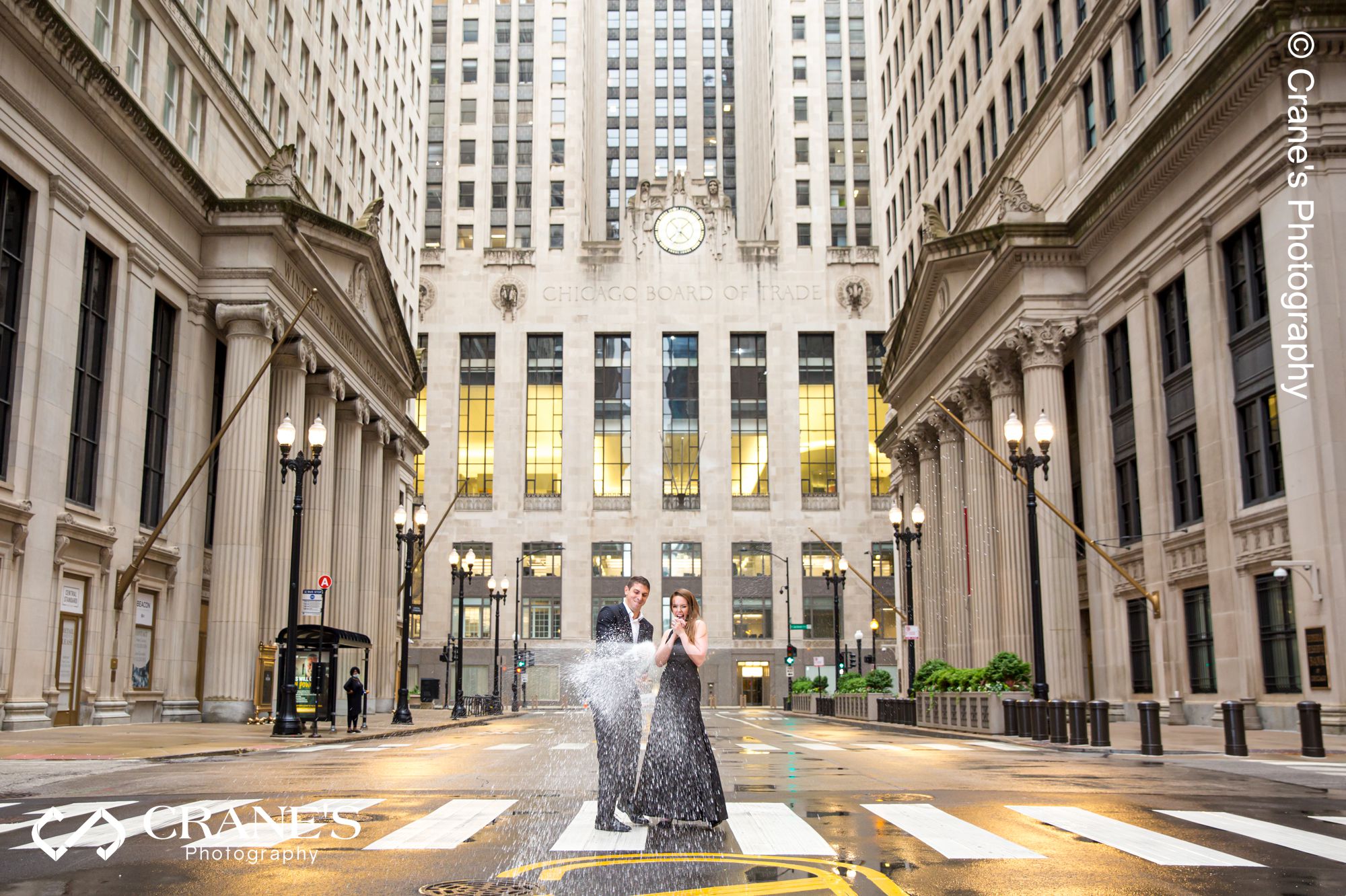 A couple in formal wear pop a champagne in front of Chicago Board of Trade Building