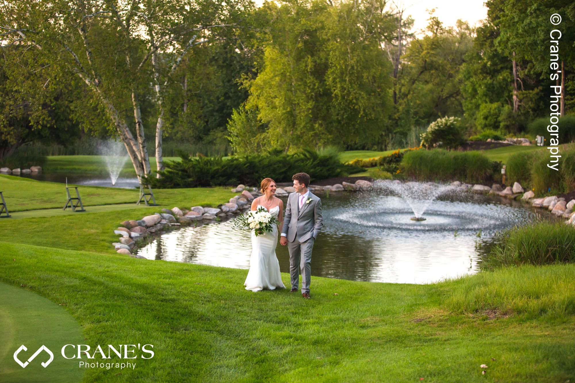 Bride and groom walking with a pretty fountain behind them at Big Foot Country Club