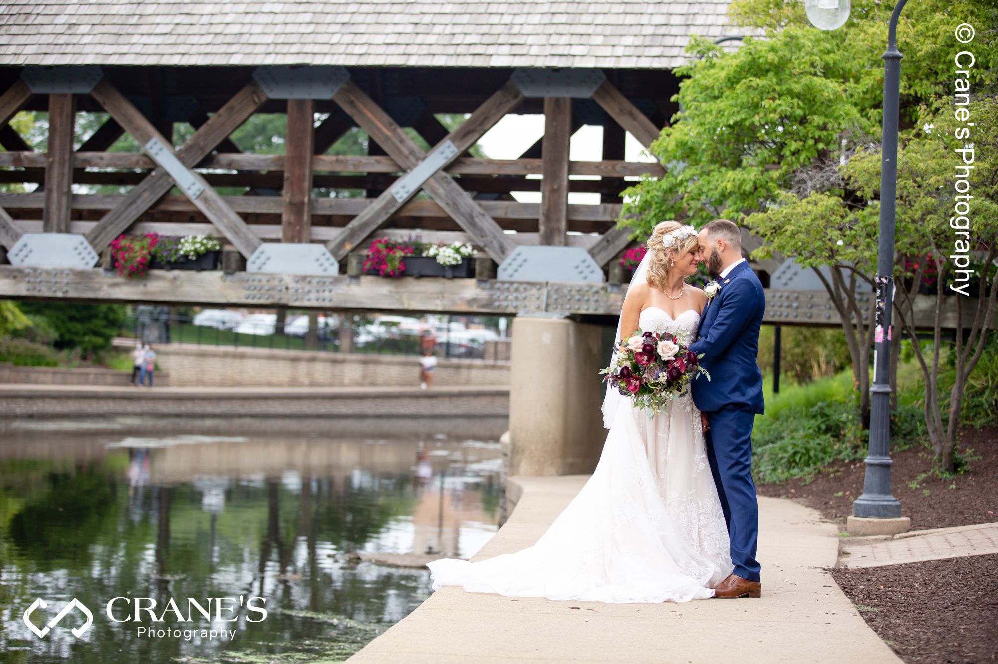 A bride and groom pose next to DuPage River just outside Elements At Water Street in Naperville