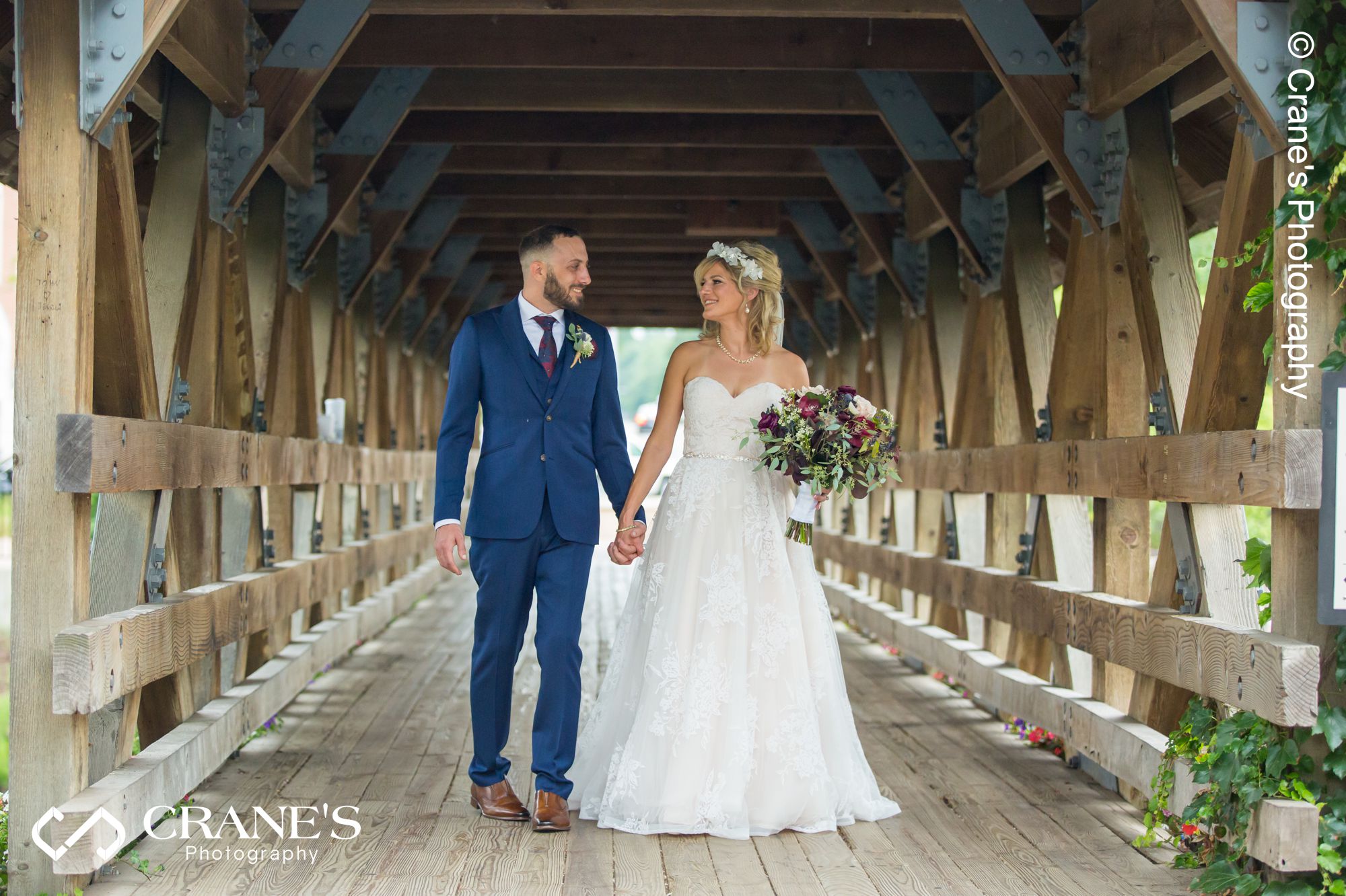 Bride and groom walk on a wooden bridge outside Elements at River Street