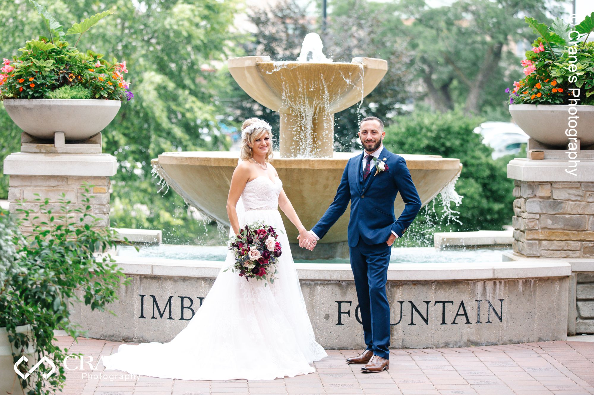 Bride and groom pose for a wedding photo in front of the fountain next to Elements at Water Street