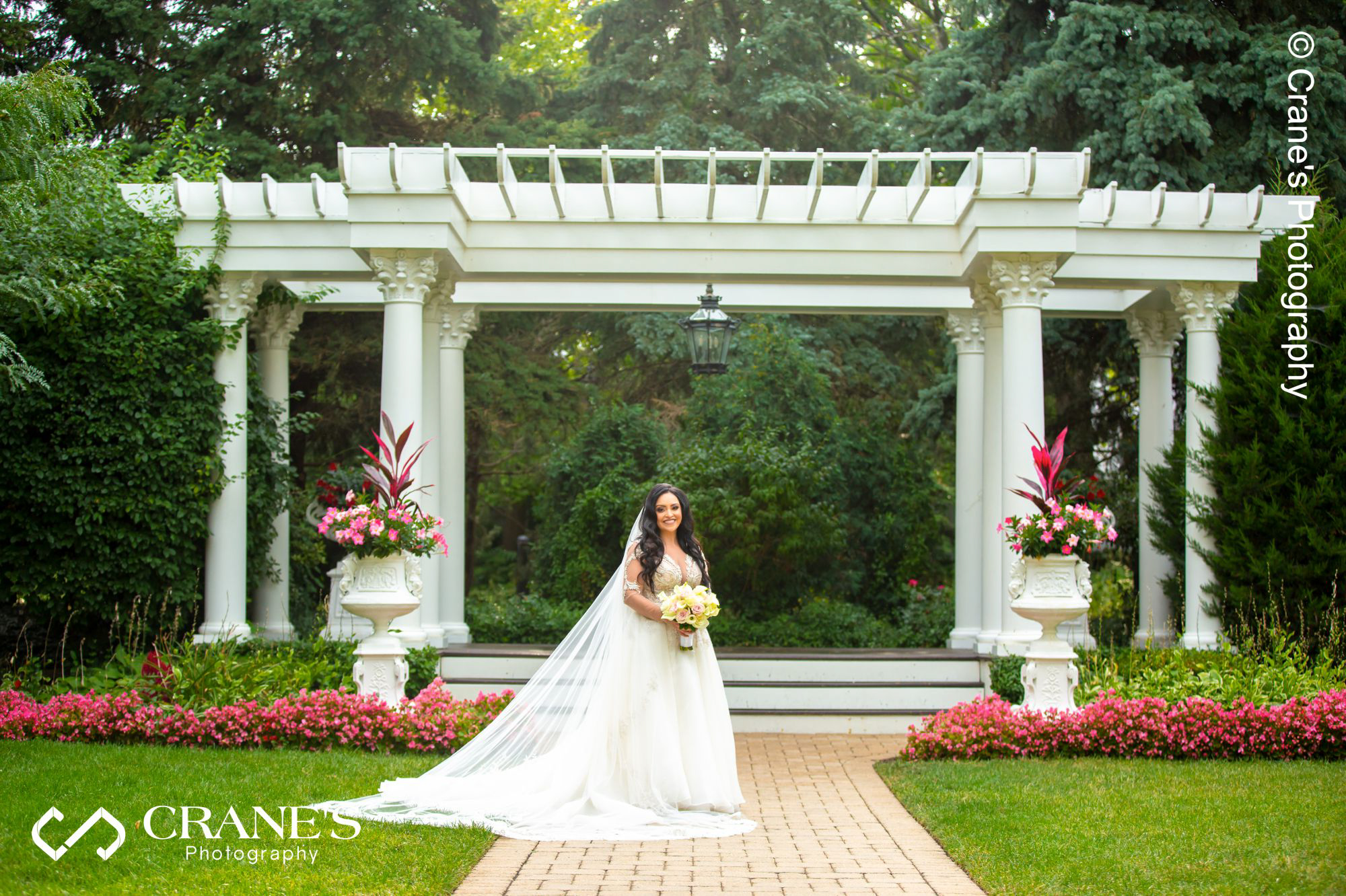 A bride with an extra long vail pose for a wedding photo in front of the pergola at Haley Mansion