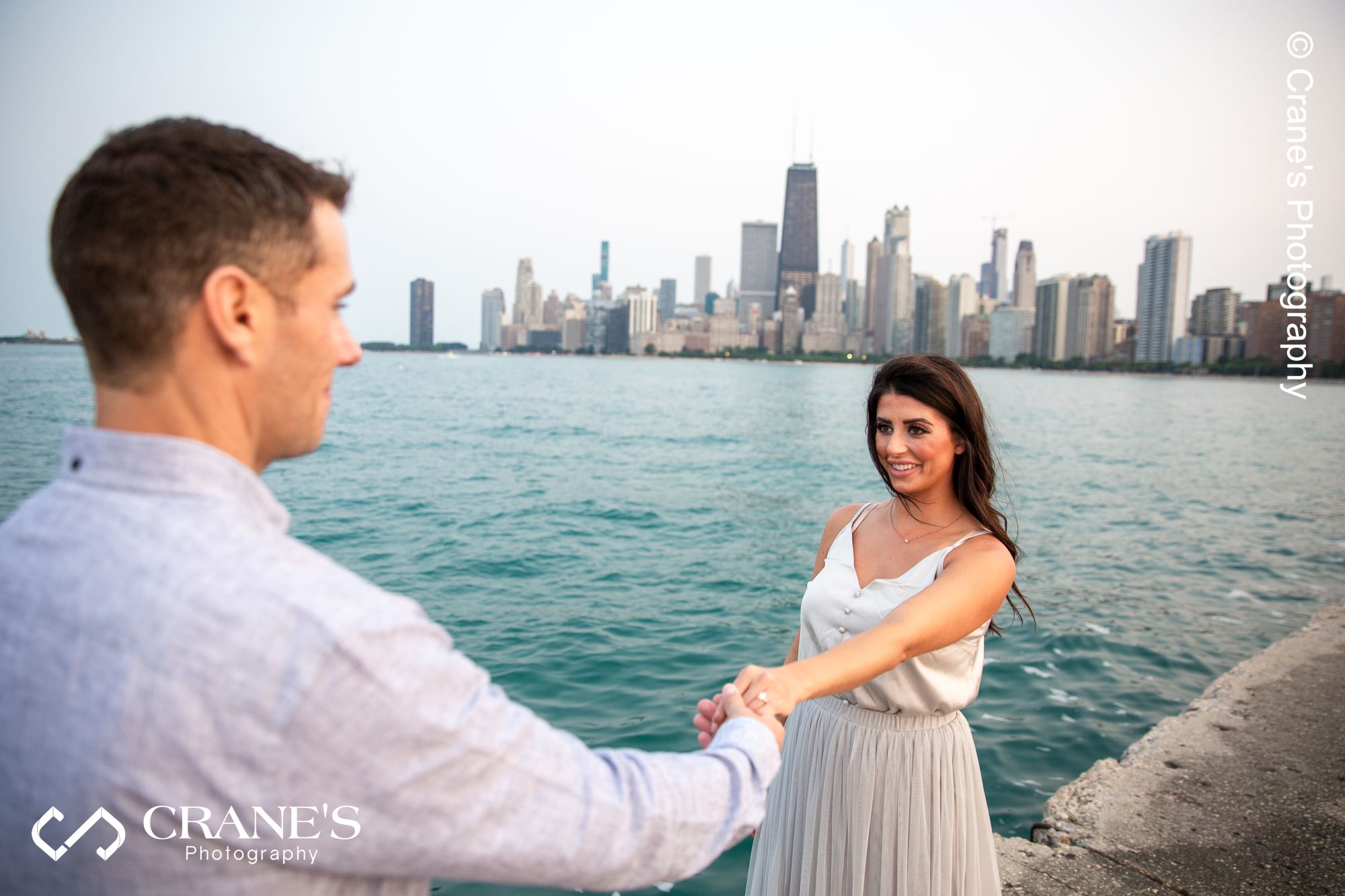 A groom-to-be is holding his fiancé's hand at their North Ave Beach engagement session
