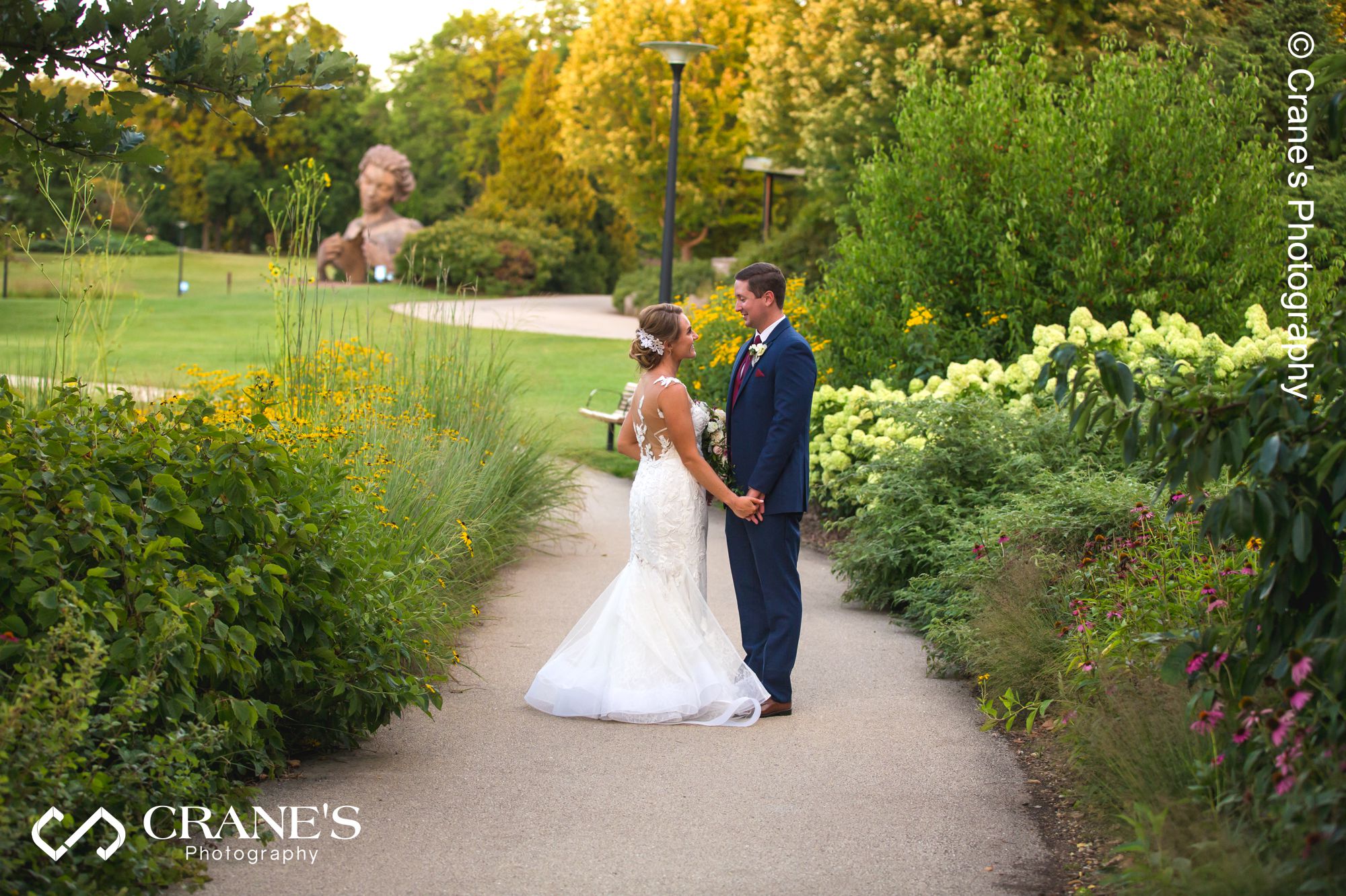 Wedding photo of a bride and groom looking at each other on a nature trail with many flowers just outside Ginkgo Room at the Morton Arboretum