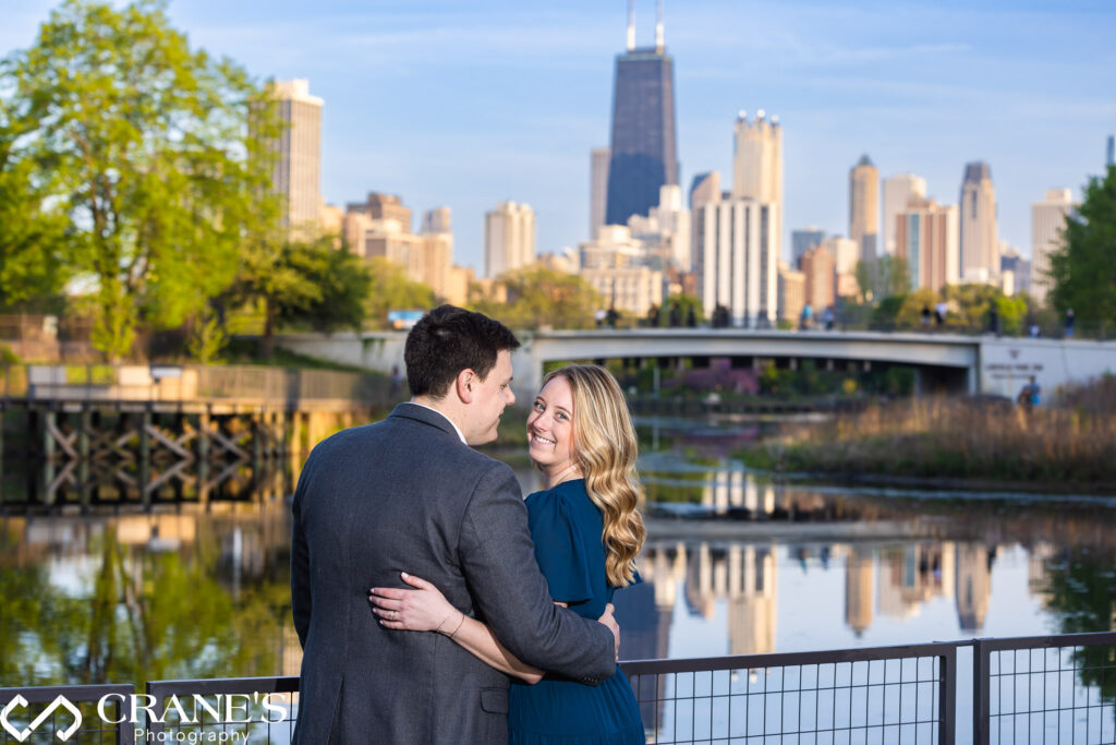 An engagement session portrait of a couple wearing blue with a great view of Chicago with all buildings reflecting over the South Pond at Lincoln Park