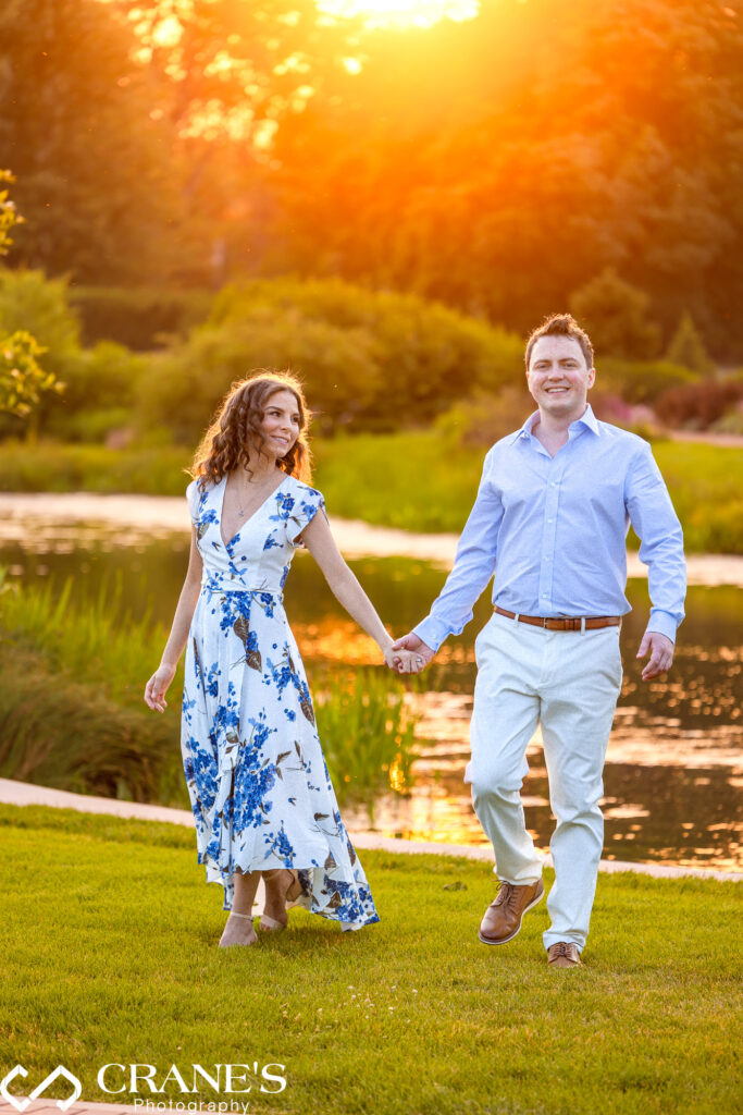 An engaged couple are walking hand in hand at Cantigny in summertime