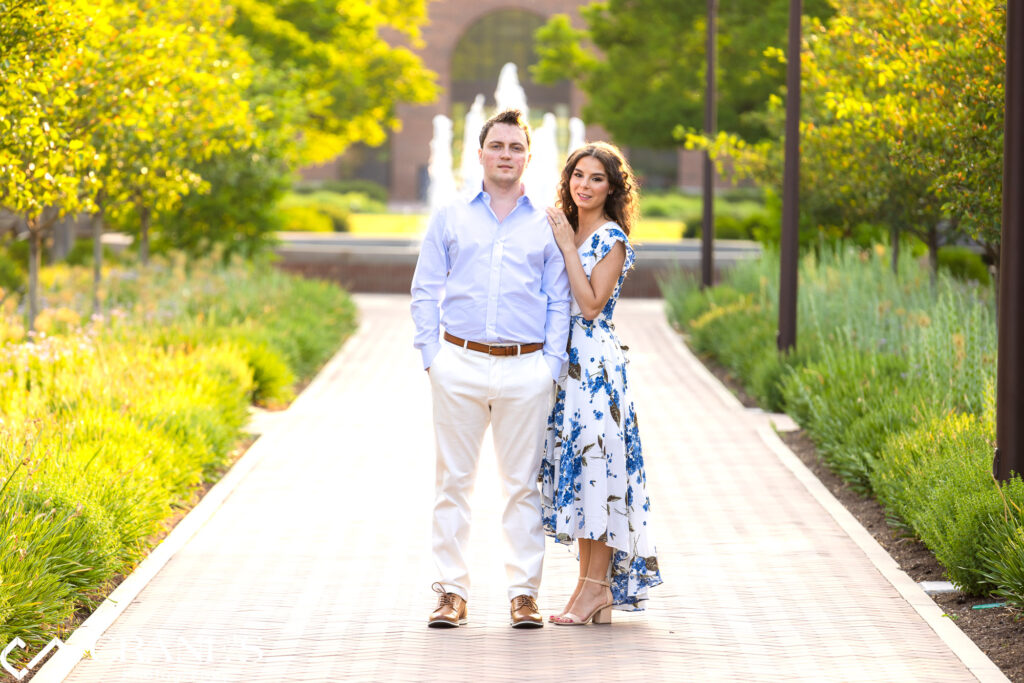 An engaged couple is posing for a photo at Cantigny park on a summer day with the fountains in the background.
