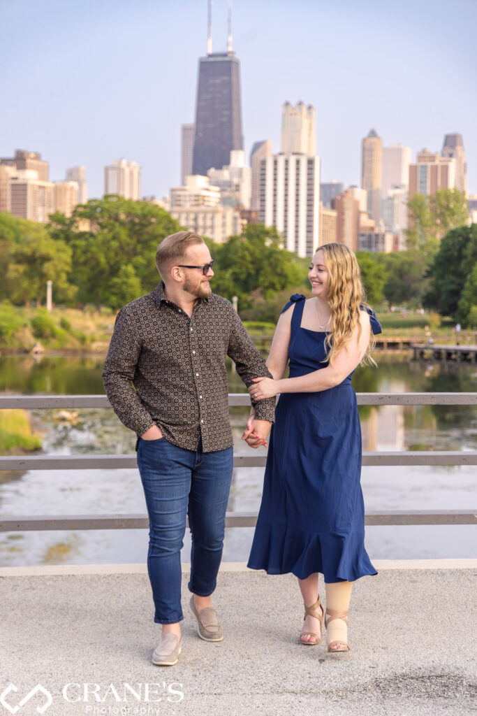 An engaged couple is walking on the bridge at Lincoln Park with Chicago in the background