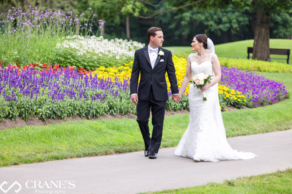 Bride and groom are walking hand-in-hand with summer flowers in the background at Royal Melbourne Country Club.