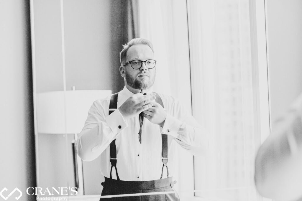 A black and white photo of a groom adjusting his tie at his hotel room at Trump Tower