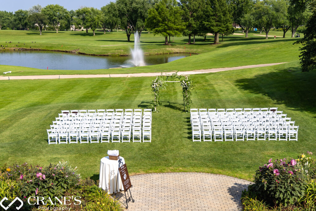 An outdoor ceremony site with white chairs and a beautiful arch with flowers at Bloomingdale Golf Club.