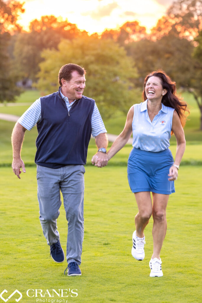 An engaged couple wearing blue sport attire are laughing together against beautiful greenery at Hinsdale Golf Club.