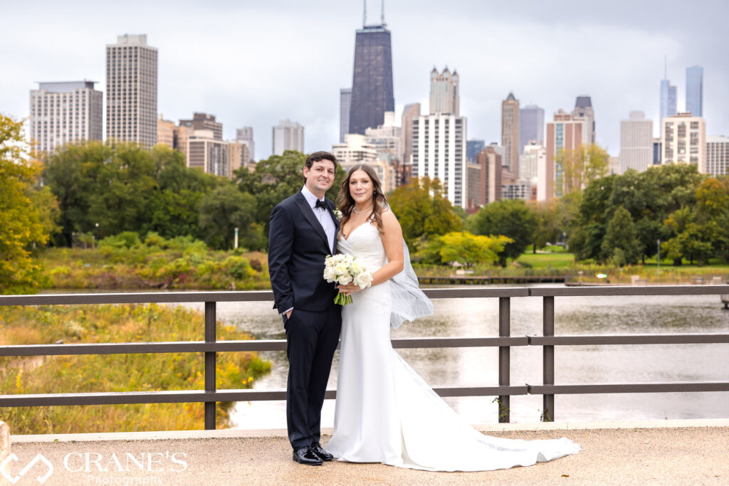 Bride and groom strike a pose on their wedding day at Cafe Brauer, framed by the backdrop of Chicago's iconic skyline