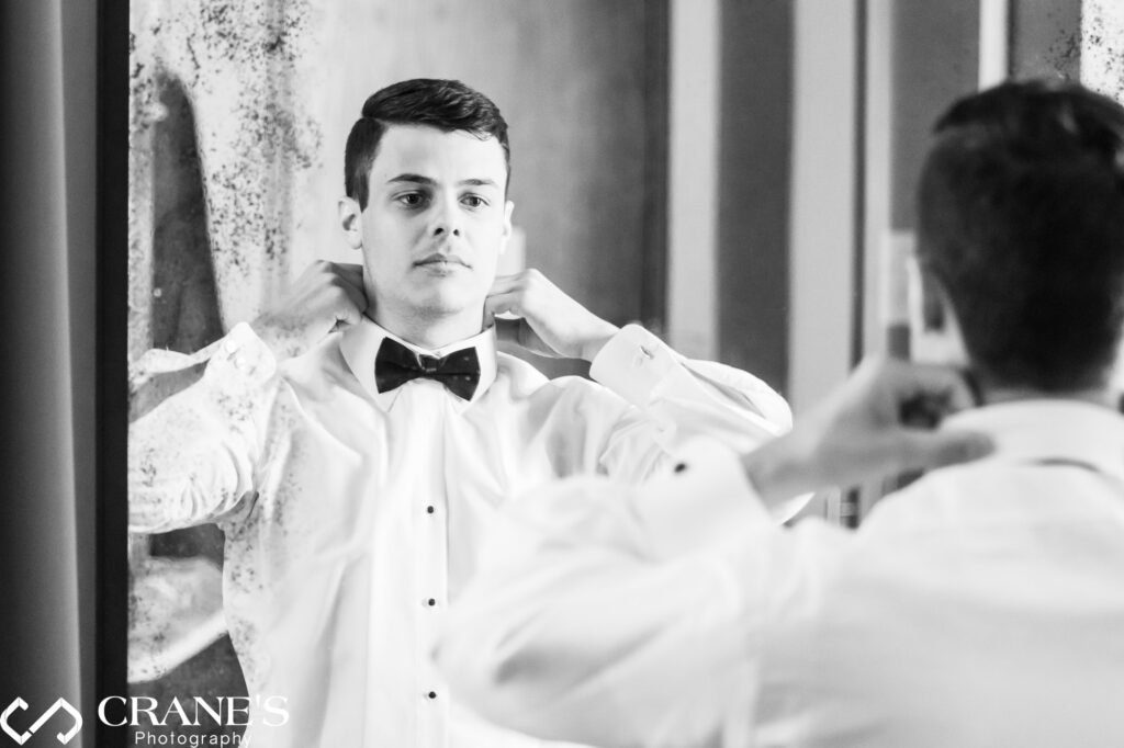 The groom is preparing for his wedding day, standing in front of a mirror in a suite at the Loews in Rosemont.