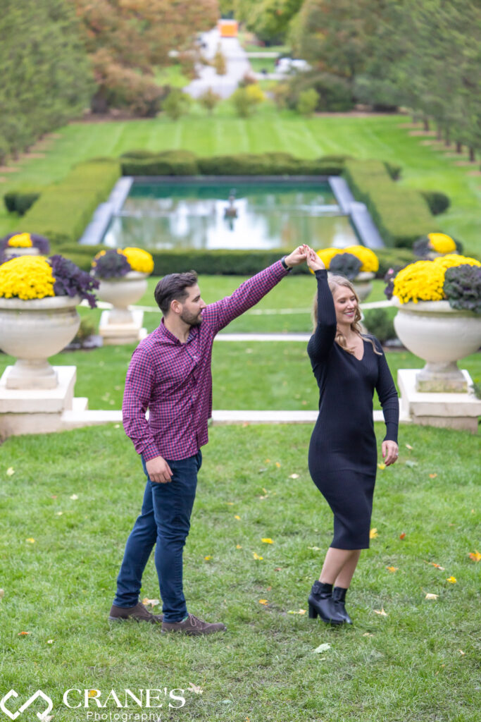 An engaged couple joyfully twirling near the Robert R. McCormick House at Cantigny Park, set against the beautiful backdrop of the fall season.