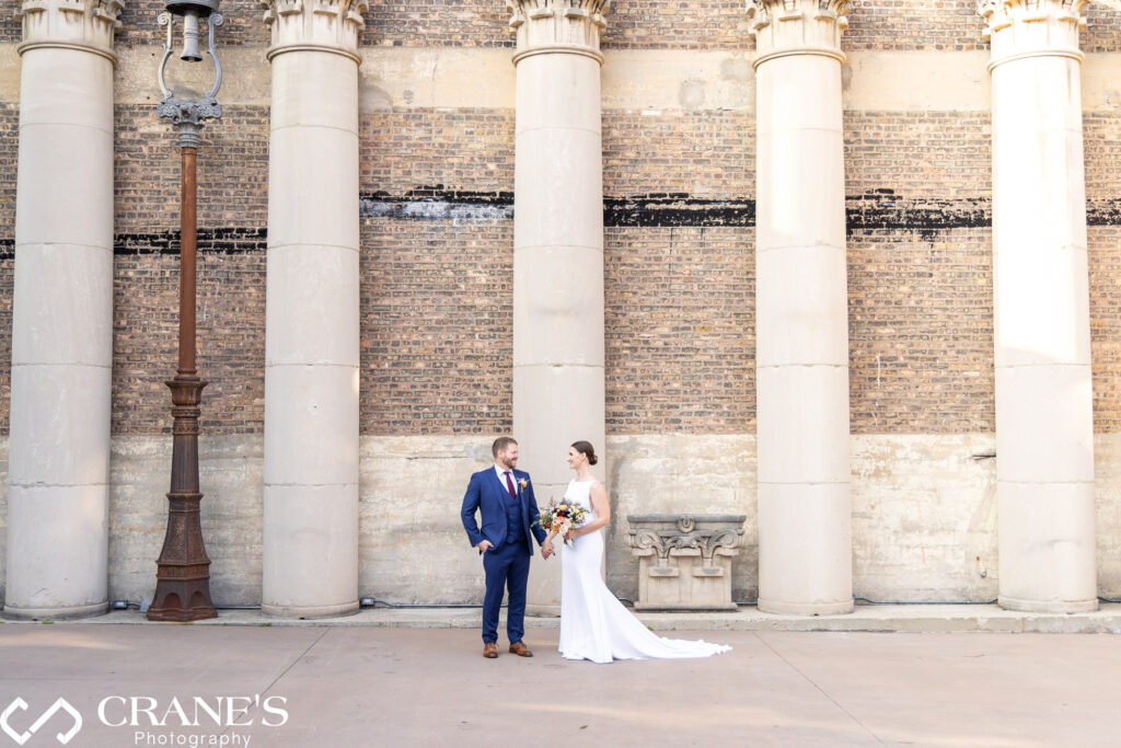 Bride and groom pose for a wedding photo at Artifact Events courtyard, framed by soaring antique stone columns.