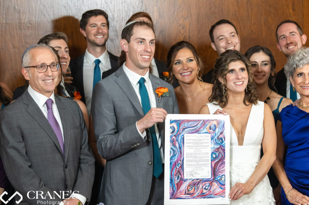 Bride and groom holding their ketubah surrounded by their family members at The North Atrium of Artifact Events.