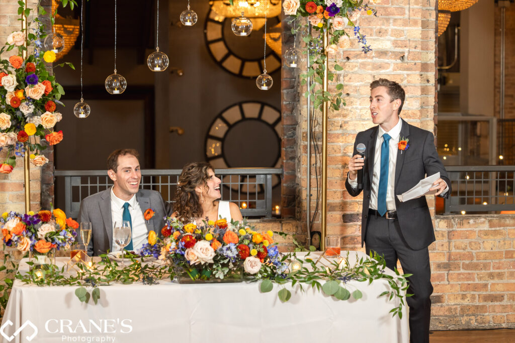 The best man delivering a heartfelt toast during a wedding reception at Artifact Events, raising a glass to honor the newlyweds.