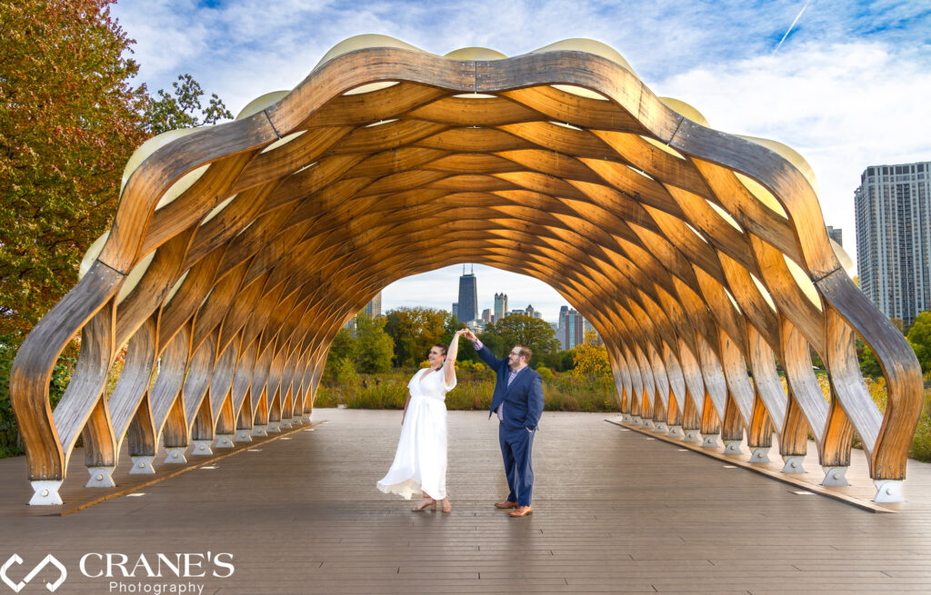 An engaged couple are having fun and twirling at the Honeycomb in Lincoln Park with the iconic skyline of downtown Chicago in the background.
