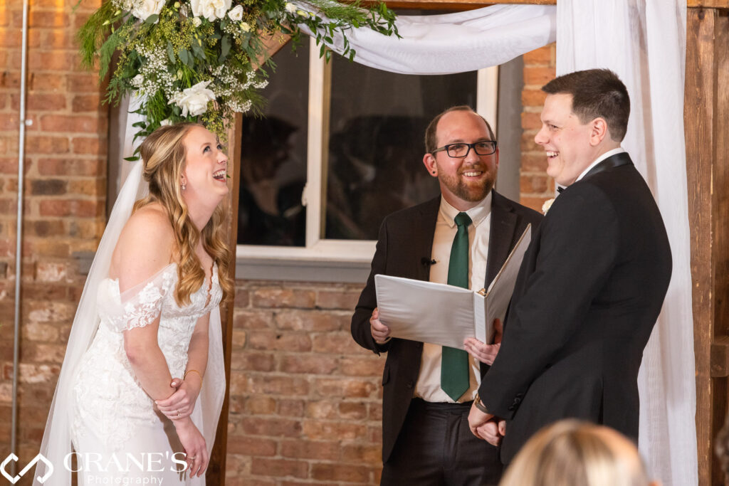 The bride and groom share laughter while exchanging wedding vows in a heartwarming indoor ceremony at City View Loft.