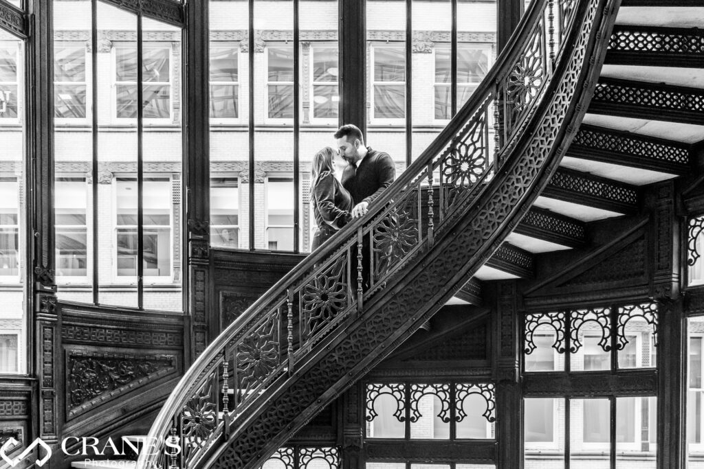 A couple shared a passionate kiss on the spiral staircase of the Rookery Building in Chicago, creating a timeless engagement session photo captured by Crane's Photography in Chicago.
