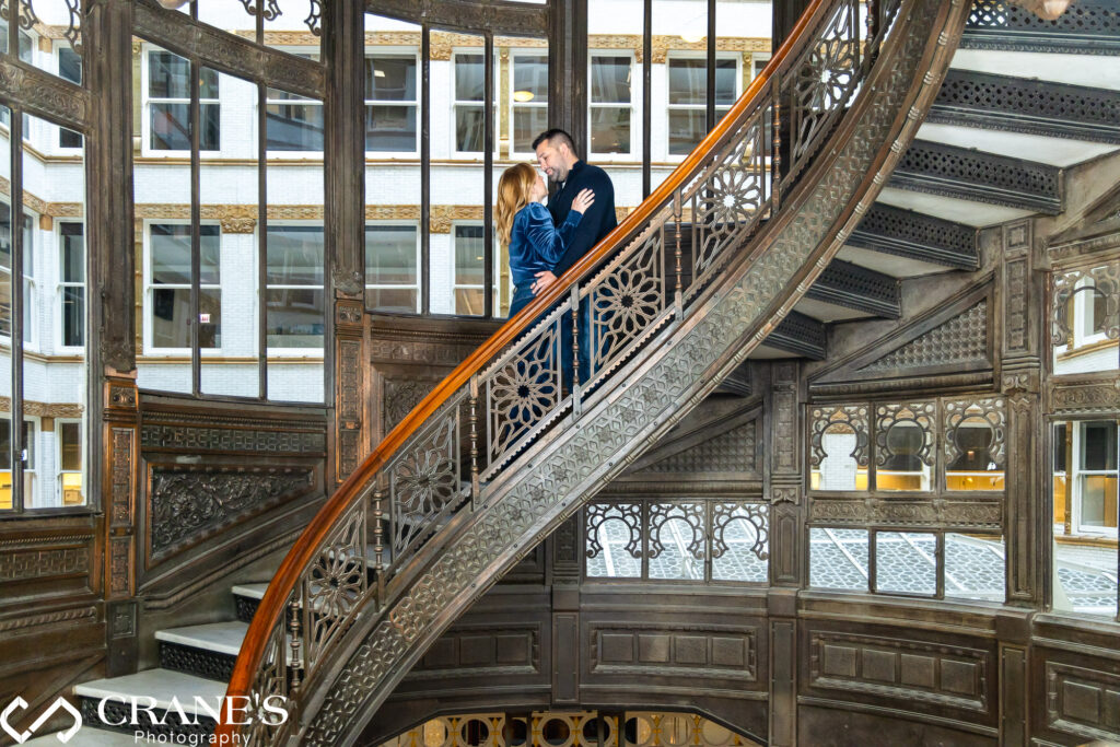 A couple joyfully poses for their engagement session photos on the captivating spiral staircase of the Rookery Building in Chicago, creating timeless memories against the backdrop of this historic architectural gem.