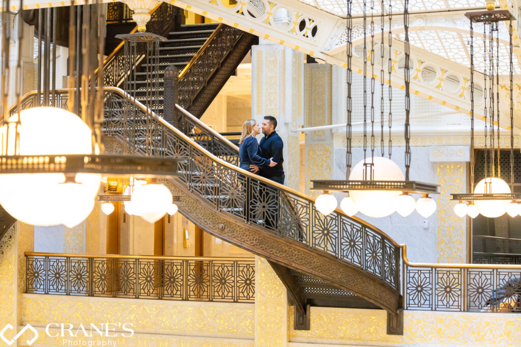 An enchanting engagement session photo taken on the stairs leading down to the Light Court at The Rookery Building in Chicago, capturing the romance and anticipation of a couple's journey together
