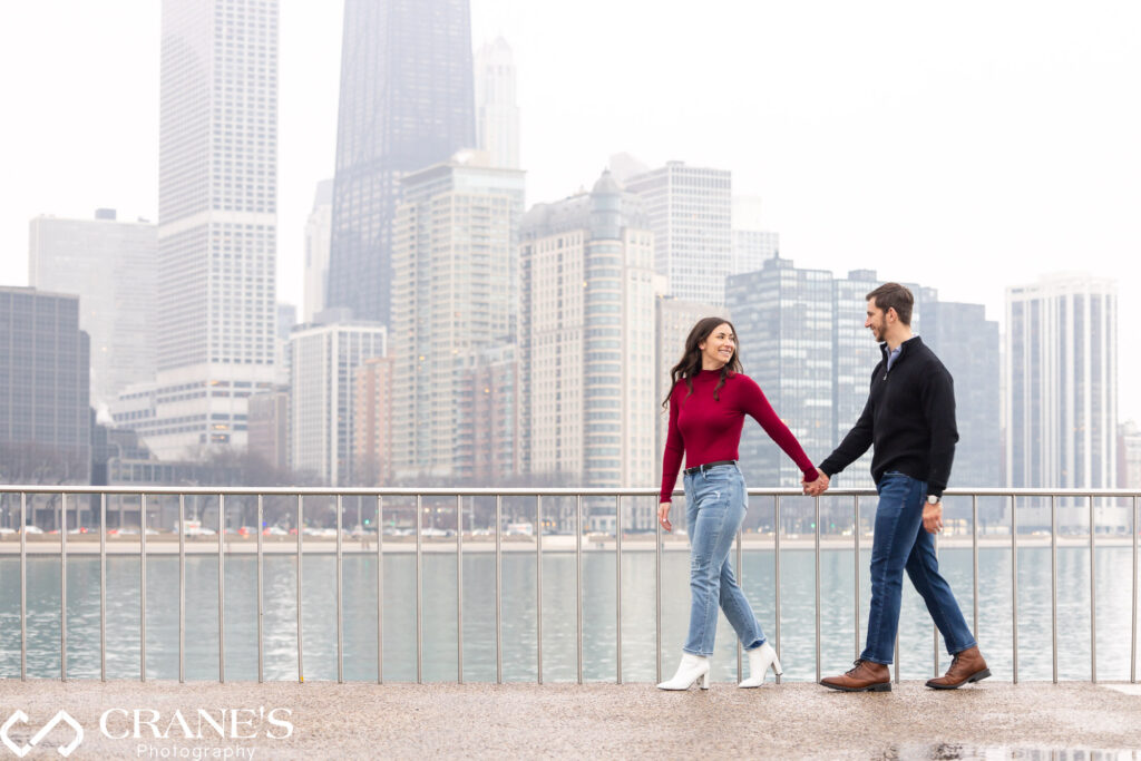 The engaged couple strolls hand in hand through downtown Chicago's Olive Park, creating a romantic scene captured during their engagement session.