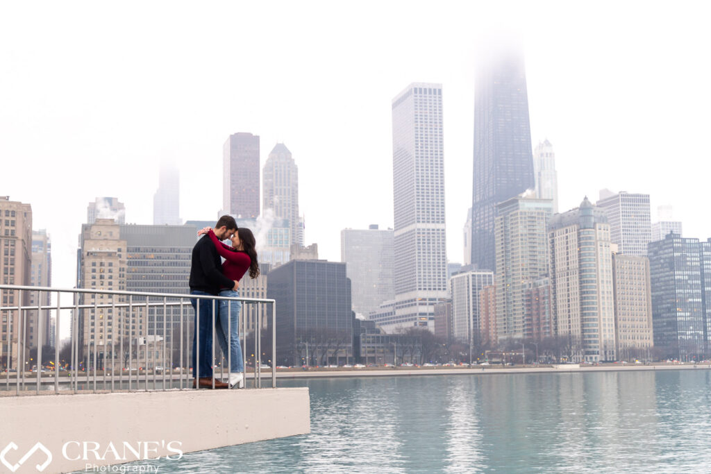 A bundled-up couple, hands intertwined, shares a loving gaze over the majestic Chicago skyline from Olive Park on a crisp winter day