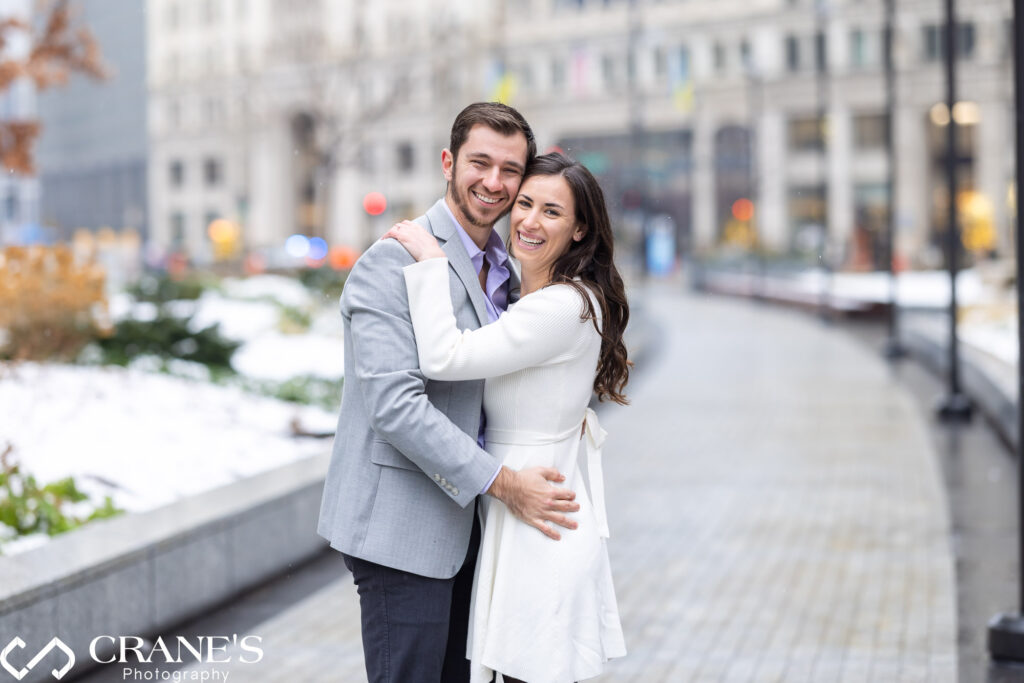 In the midst of a winter wonderland in downtown Chicago, a beaming engaged couple embraces with pure happiness, sharing radiant smiles for the photographer capturing the warmth of their love.