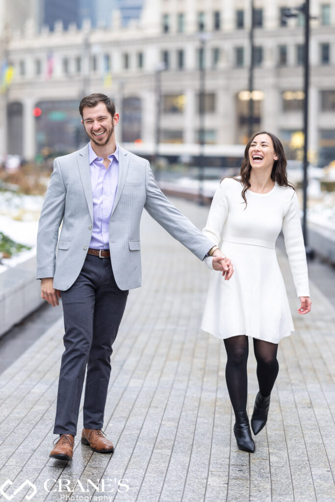 In a snowy downtown Chicago engagement session, the couple shares laughter, with the iconic Wrigley Building in the background, creating a joyful and charming winter scene.
