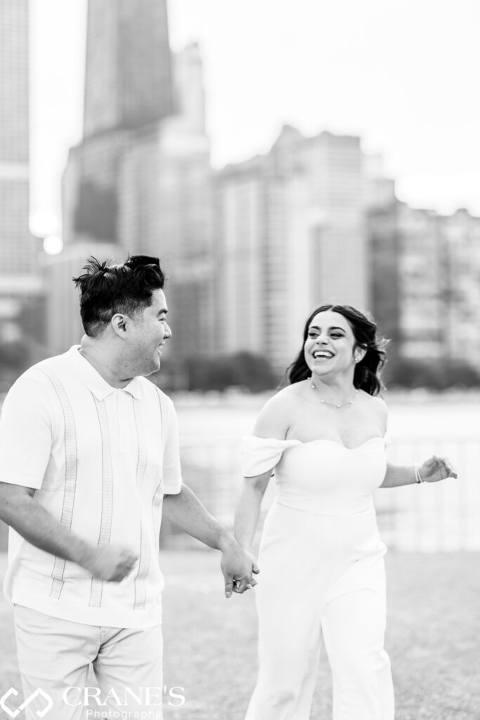 An action shot of an engaged couple running at Olive Park. They hold hands and their smiles are radiant with joy and excitement. In the background, the iconic skyline of downtown Chicago adds to the energy of the moment.