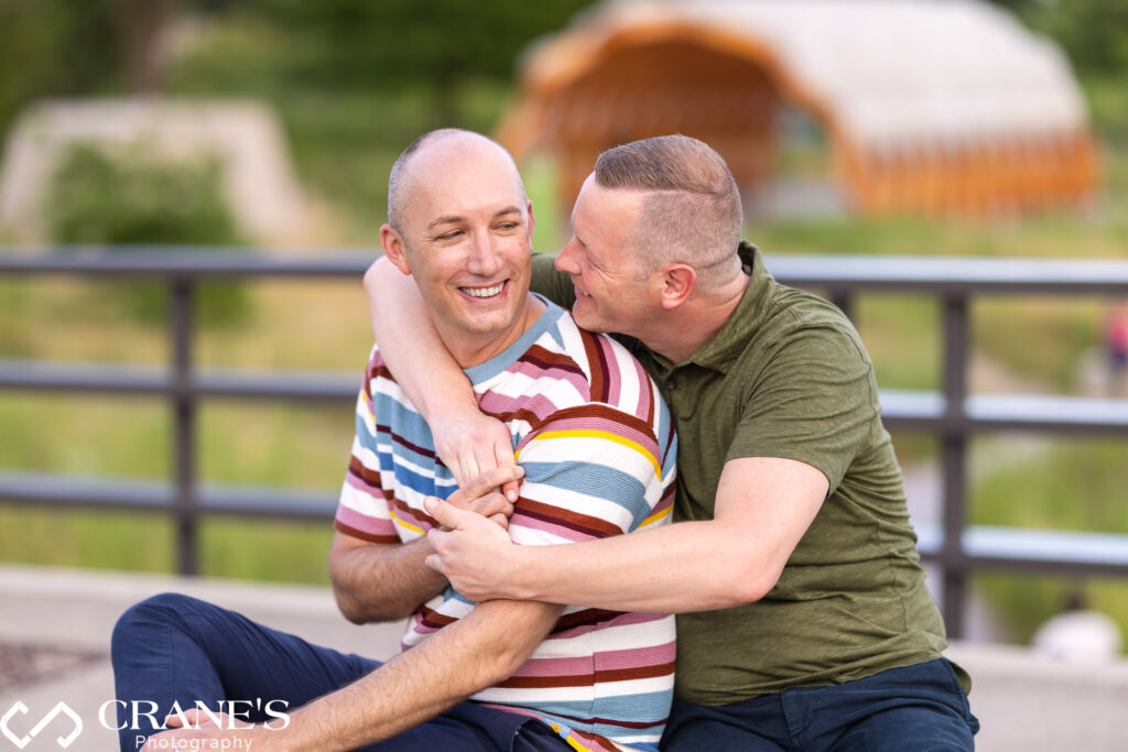 Two men hugging and visibly happy during their LGBTQ+ engagement session at a bridge overlooking the South Pond in Lincoln Park, Chicago.