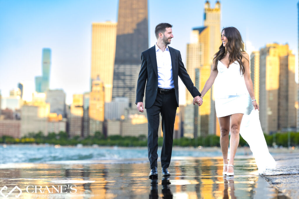 A stunning engagement photo at North Ave Beach of a couple walking hand in hand, elegantly dressed.