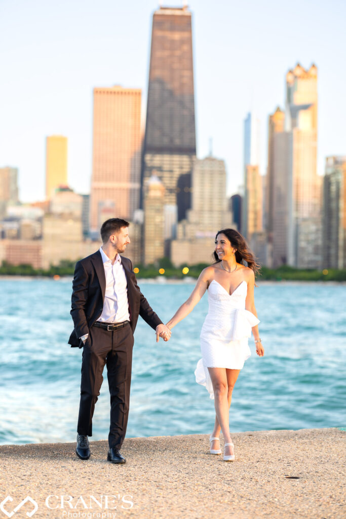 An elegantly dressed couple, the woman in a stunning white dress and the man in a sharp black tuxedo, share a loving moment during their engagement shoot at North Avenue Beach, Chicago.