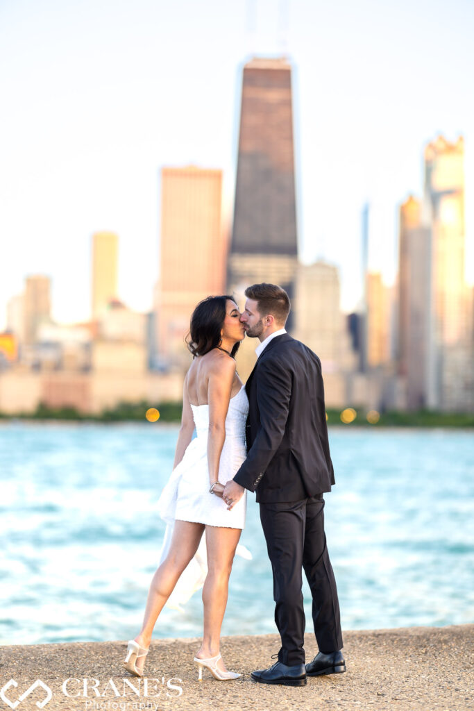 An elegantly dressed couple, lost in a kiss, celebrates their engagement on North Avenue Beach. The warm glow of sunset paints the Chicago skyline in a romantic hue.