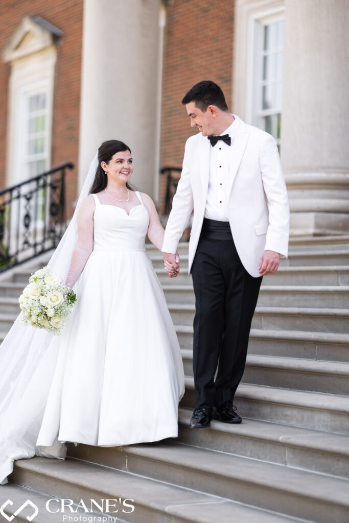 A soft, award-worthy wedding photo of a radiant bride and groom in elegant attire, walking down the grand staircase of the Chicago History Museum.