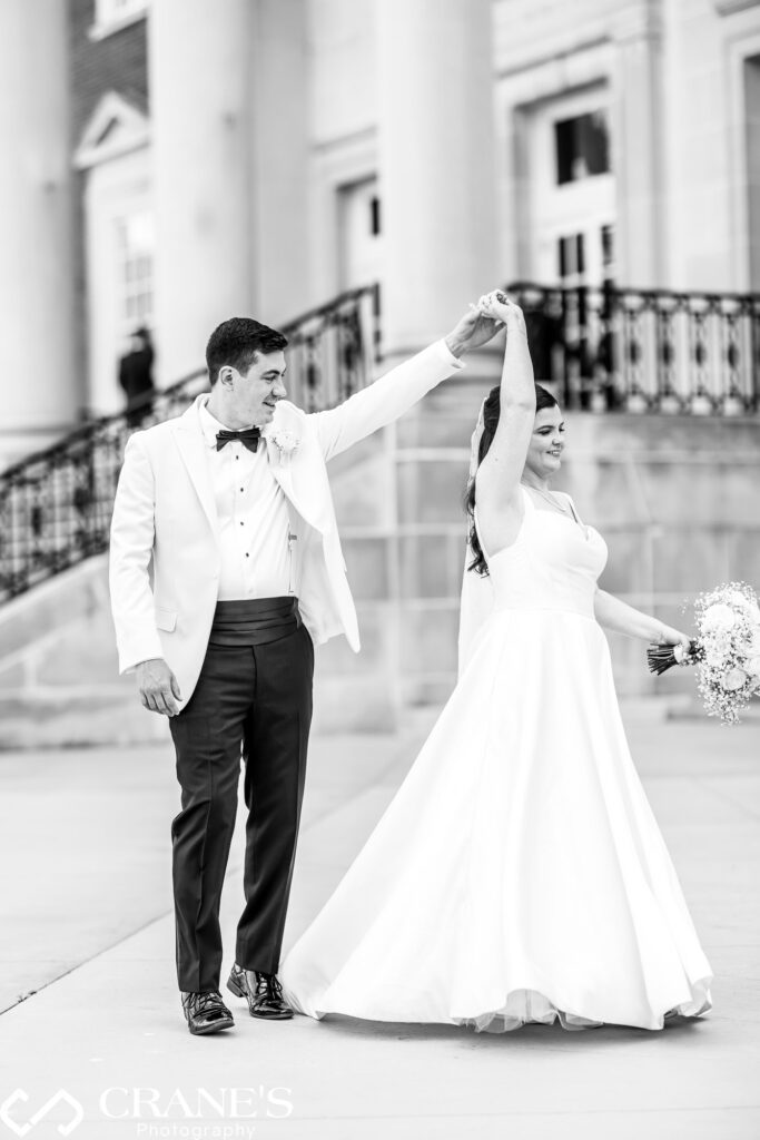 A groom twirls his bride on their wedding day at Uihlein Plaza at the Chicago History Museum. The bride's dress flows gracefully as they share a joyful and romantic moment against the beautiful outdoor setting of the historic venue.