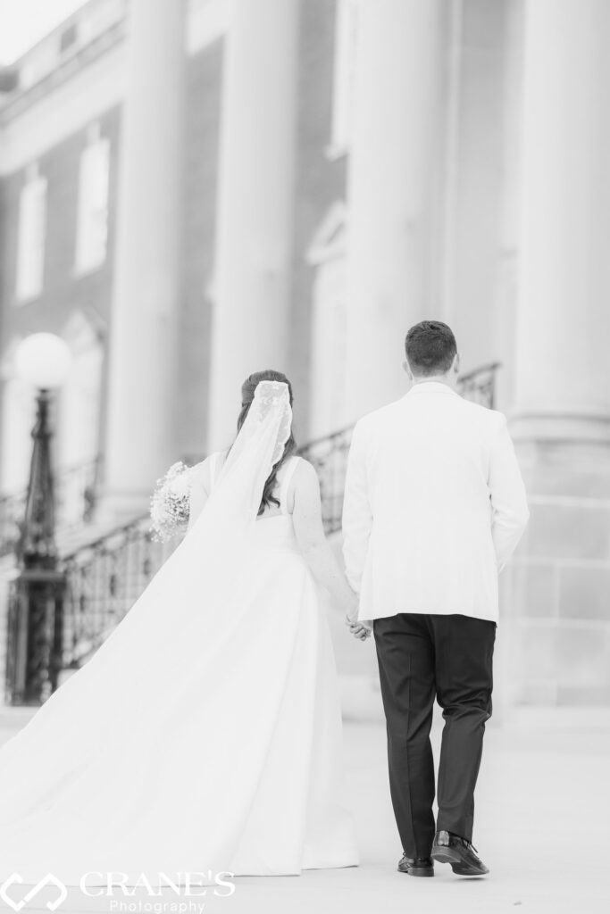 A black-tie couple walking towards the grand staircase of the Chicago History Museum. The bride's train flows gracefully behind her. A timeless, award-worthy wedding portrait.