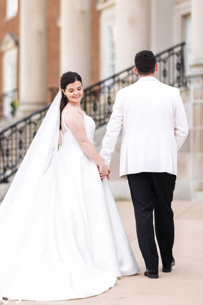 Elegant couple ascends Chicago History Museum's grand staircase on wedding day. Bride, turning back, admires flowing train. Timeless scene.