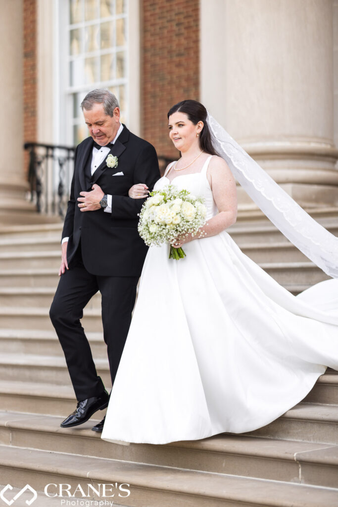 The bride and her father walk down the aisle during an outdoor wedding ceremony at the Chicago History Museum. The bride, in her elegant gown, holds her father's arm as they share this heartfelt moment.